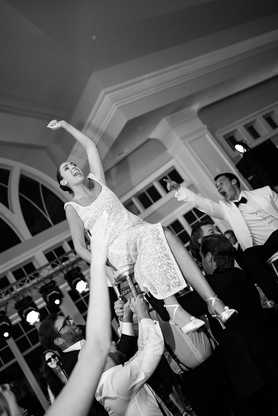 Black and white film photo of the bride cheering enthusiastically while lifted in a chair during the Hora.